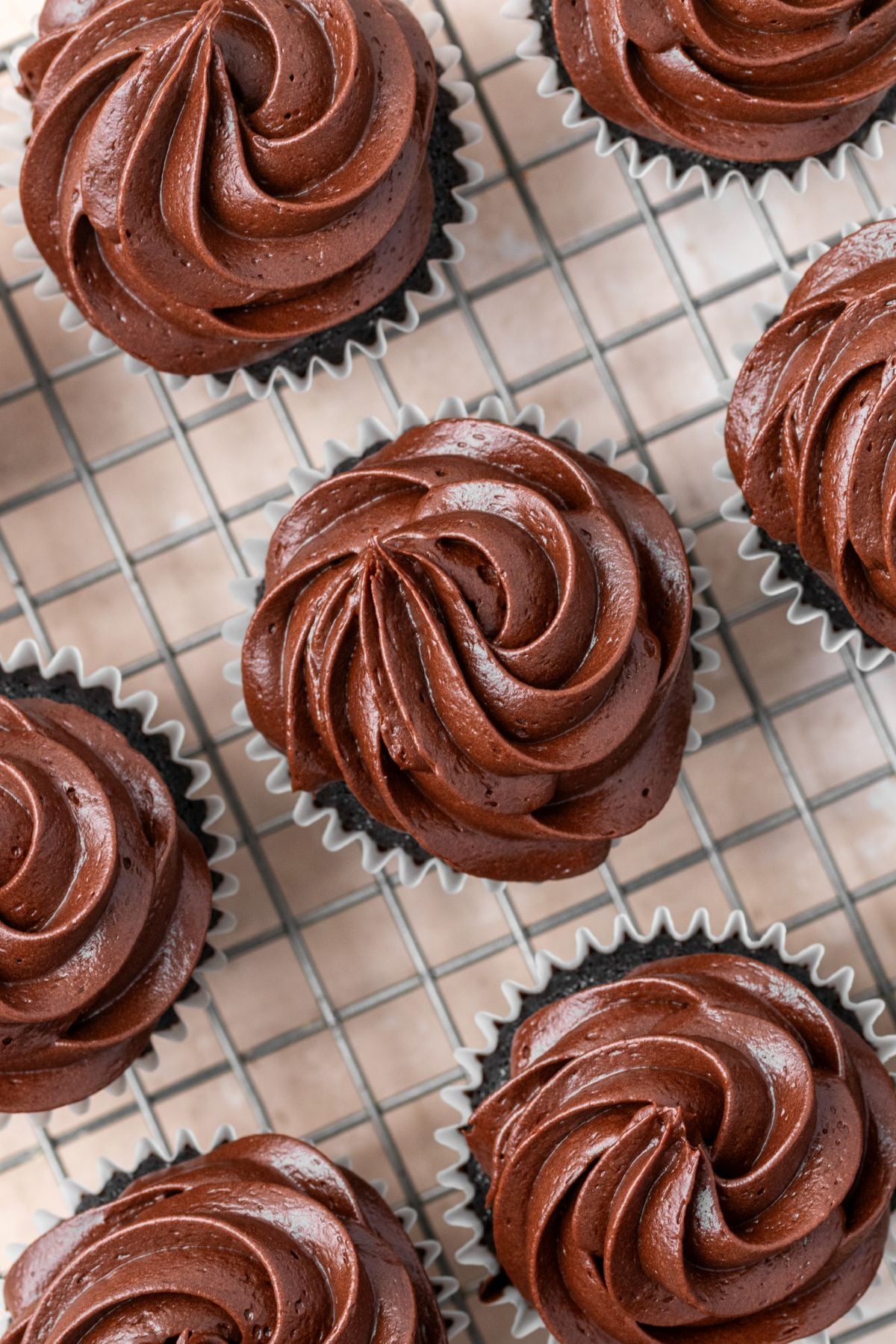 Chocolate cupcakes on a wire rack topped with chocolate cream cheese frosting.