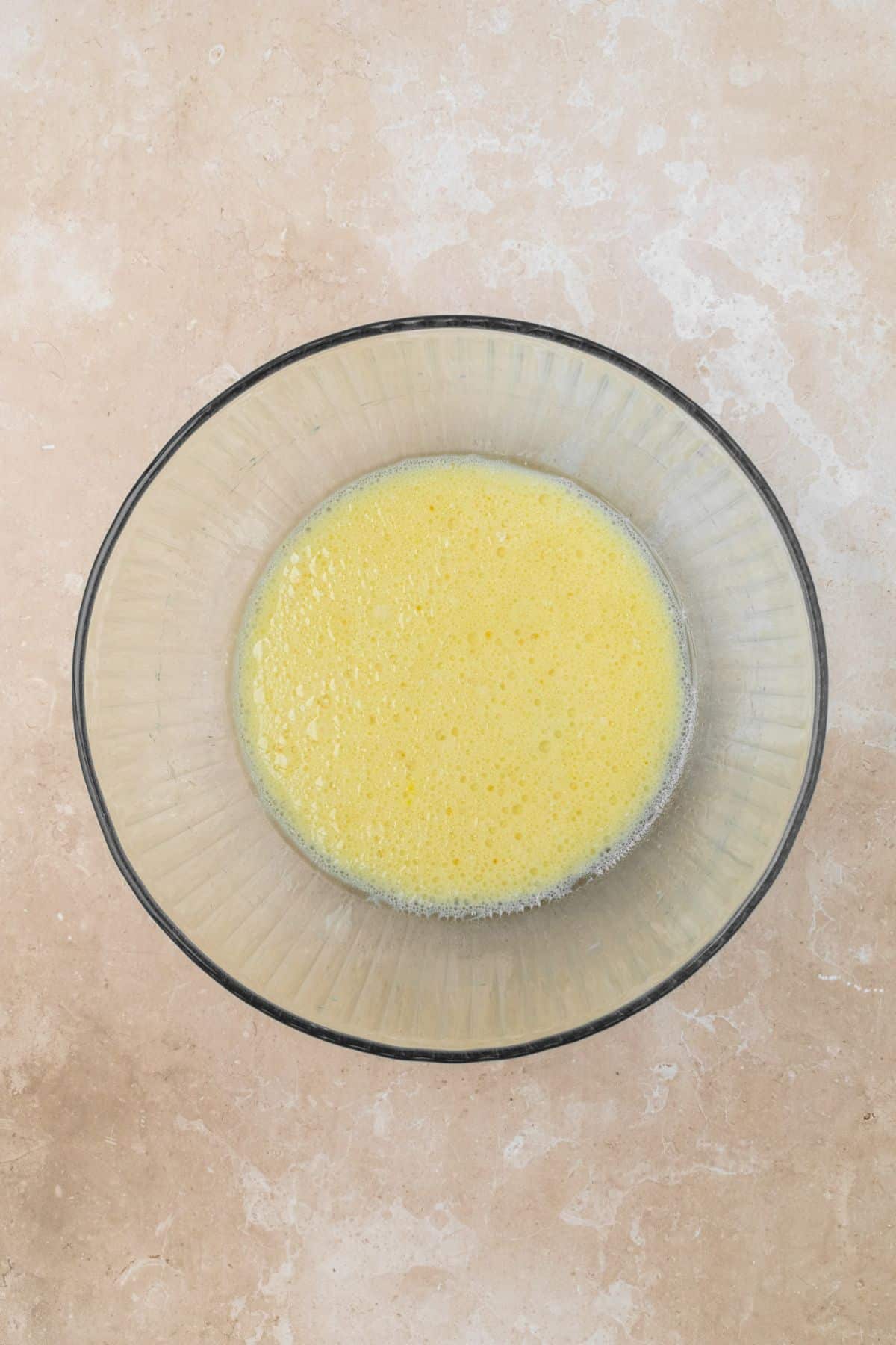 Sugar, milk, oil, and egg whisked together in a large glass bowl.