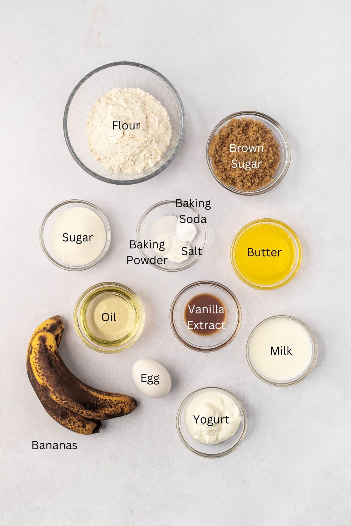 Ingredients for banana cupcakes: flour, sugars, butter, oil, baking powder, baking soda, salt, egg, yogurt, milk, and bananas.