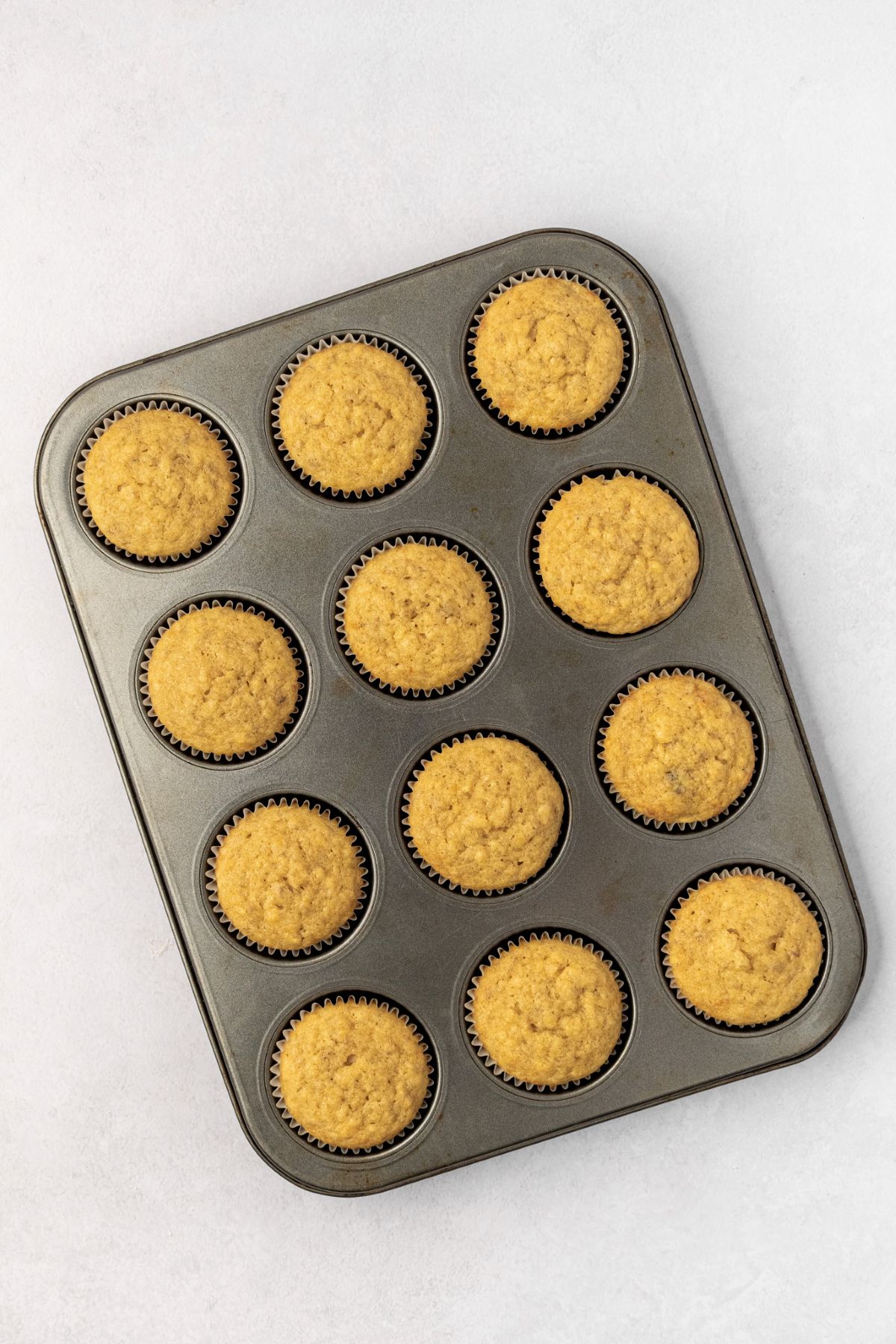 Baked and cooled banana cupcakes in a muffin pan.