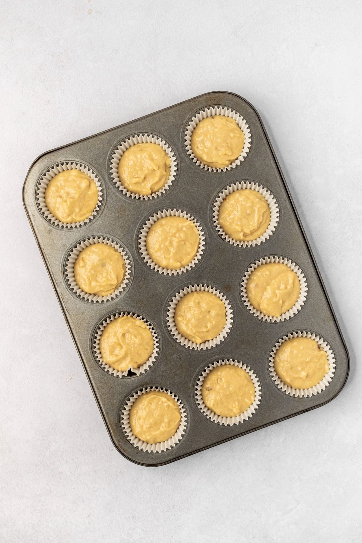 A muffin pan lined with cupcake liners and filled with banana cupcake batter.