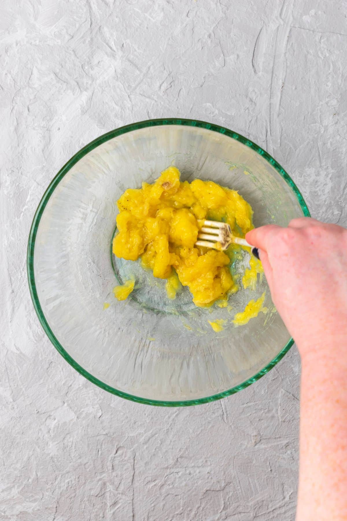Mashed banana in a large glass mixing bowl.