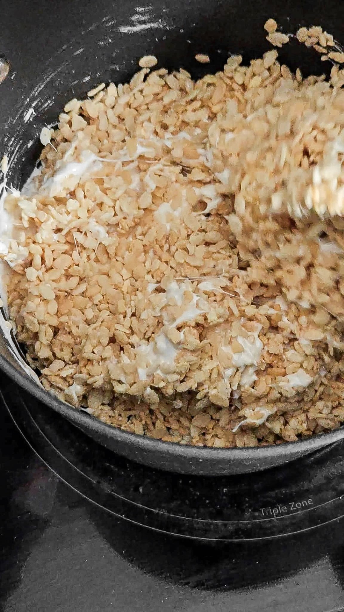 Rice cereal mixed into melted marshmallows in a large saucepan.