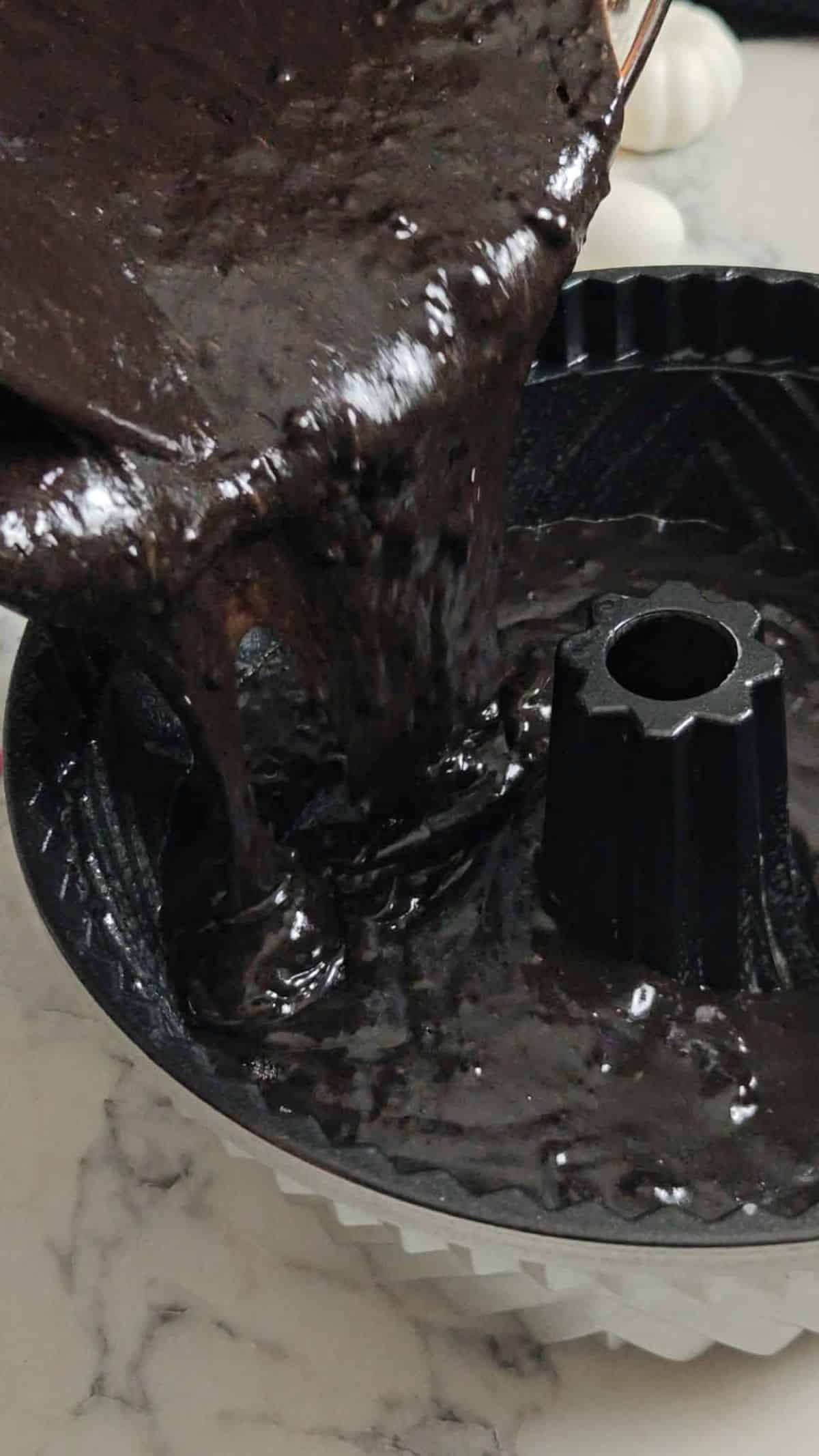 Chocolate cake batter being poured into a bundt pan.