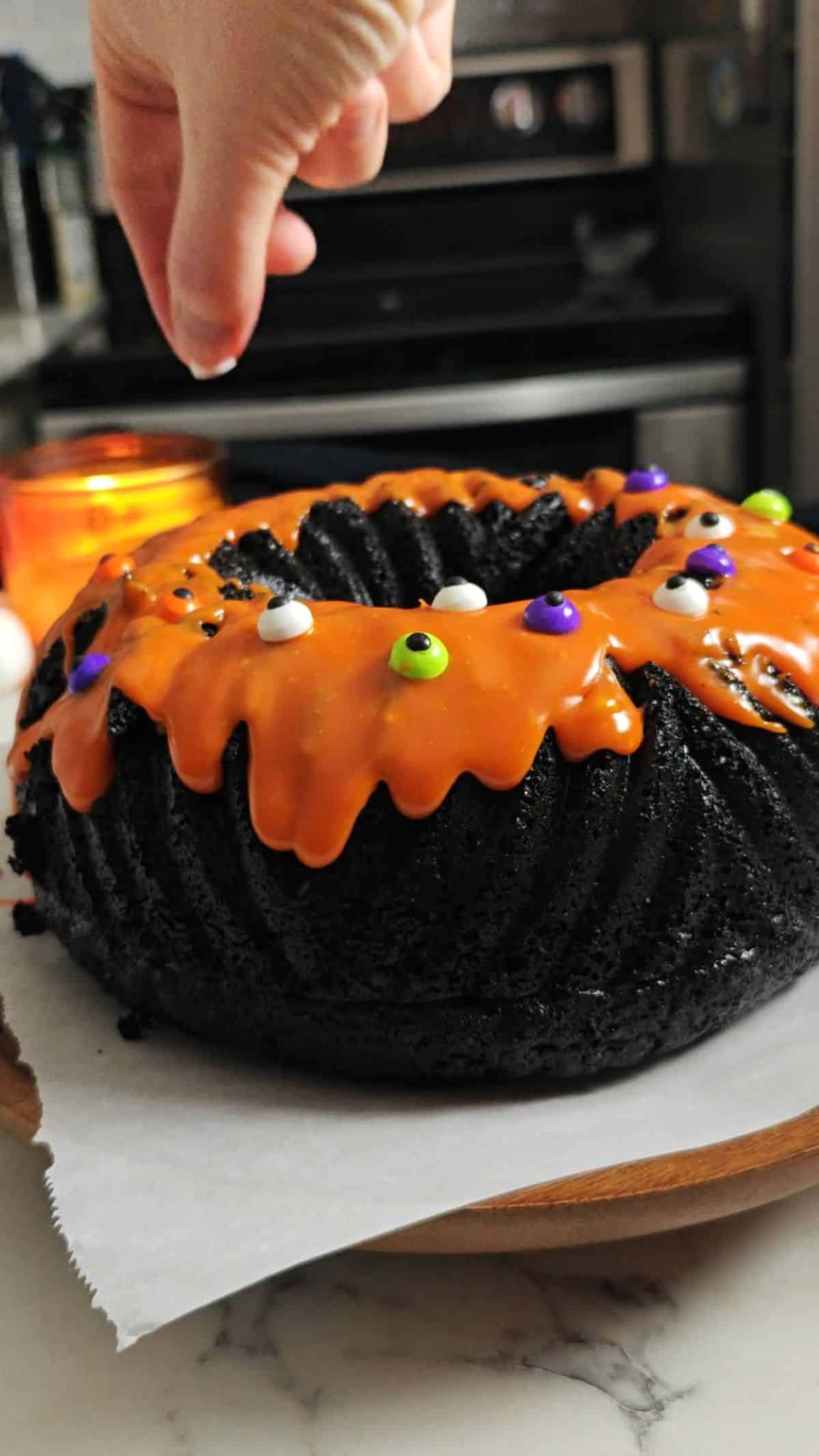 A black cake with orange white chocolate icing and eyeball sprinkles.